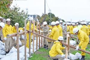 黄色い作業服を着て杭を打つ水防団員たち