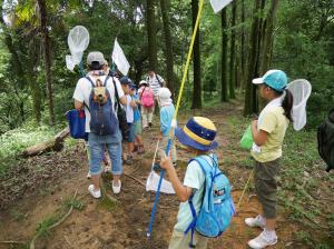 虫カゴと虫網を持ち木々の中に集まる子どもと大人