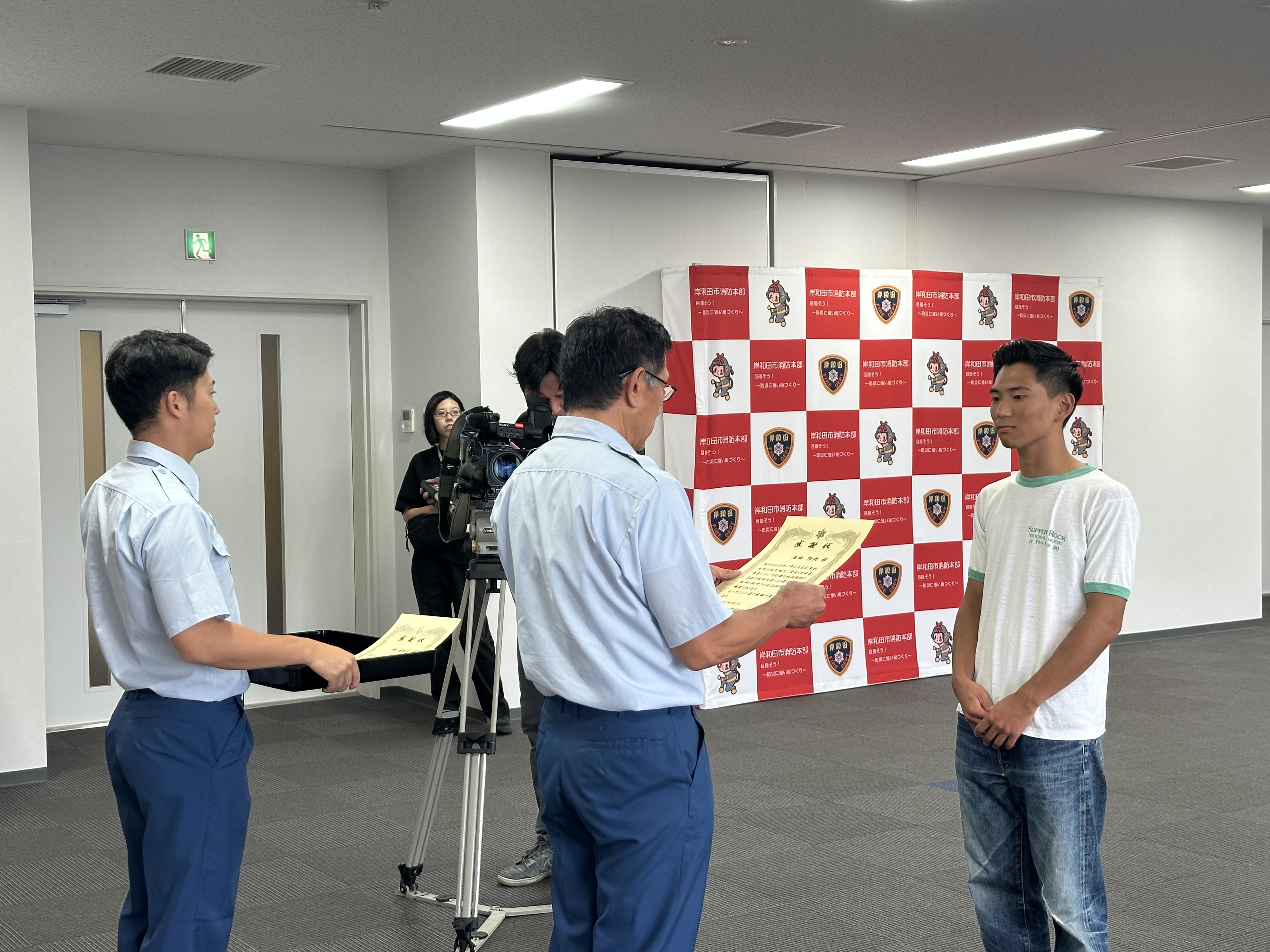 消防長から感謝状を読み上げ男子大学生に渡す写真