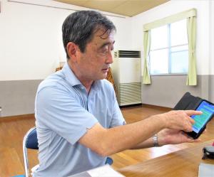 携帯電話を指してLINEの活用について説明する中野会長の写真