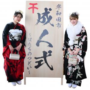 成人式の看板の横に立つ振り袖姿の成人女性2人