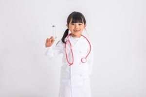 白衣を着て聴診器を首にかけ、右手で注射器を持つ小学生の女の子