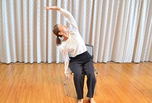 イスに座って左手を頭の上に伸ばす講師の西村先生