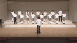 制服を着た16人の学生が舞台で合唱を発表している様子