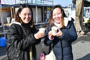 牡蠣味噌汁が入った紙コップを持って笑顔の女性二人