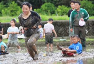 ドロドロの田んぼで女の子が小さな男の子が乗ったそりを引っ張る様子