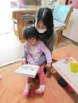 女性の膝の上に座り絵本を見る子ども