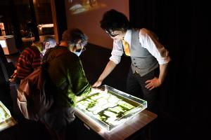 サンドアートを体験する高齢の女性とアドバイスするkoheiさん