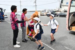 バスから降りてくる子どもたちをタッチで出迎えるセレッソ大阪アンバサダーの男性2人と公式キャラクターのロビーくん