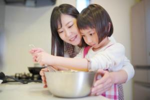 真剣な表情で泡だて器を持つ女の子とボウルを支えてあげるお母さん