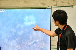画面に映るシリヤケイカの説明をする柏尾学芸員