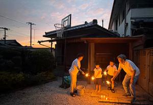 夕暮れ時に家の庭で花火をするおじいさん、おばあさんと孫ふたり