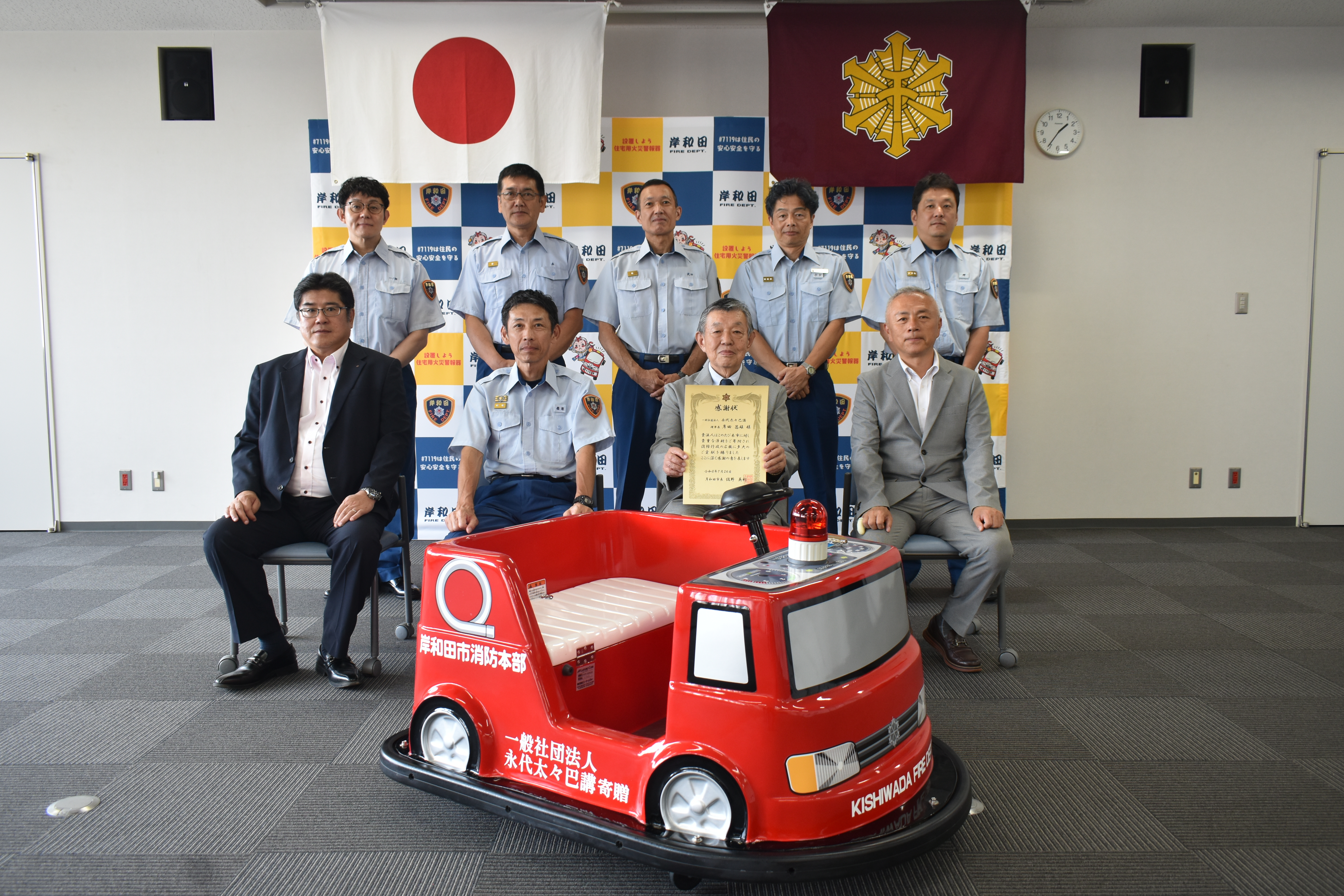 寄贈頂いたバッテリーカーと巴講の3名、消防長以下課長との集合写真