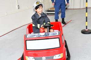 防火衣を着てヘルメットを被って消防ミニカーに乗る男の子