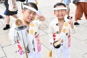 お揃いの白い法被を着て、ミニ纏を持つ幼い男の子ふたり
