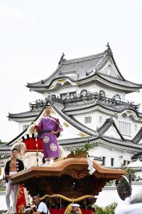 お城と本町のだんじり（大屋根に紫色の着物を着た大工方の男性）