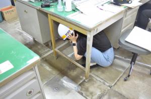 ヘルメットをかぶり机の下に隠れる様子