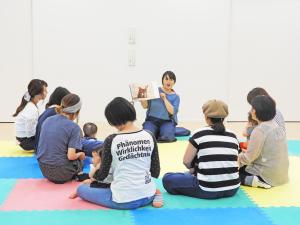 絵本を読む人の周りに座る親子