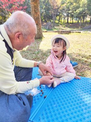 シートの上で向かい合って笑顔で座るおじいさんと子ども